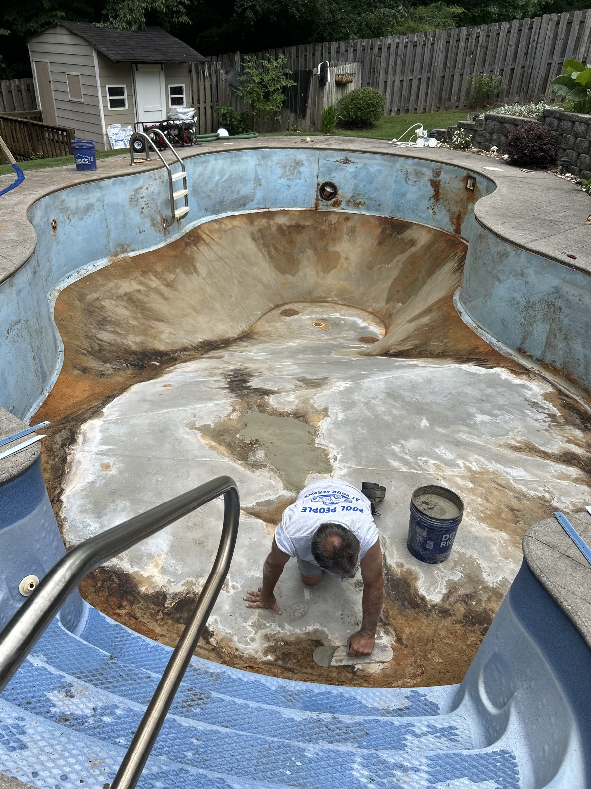 Rust-stained cloverleaf pool shell being prepped by a Pool People technician before a new liner