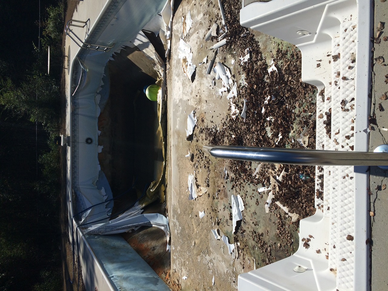 In-ground swimming pool with a torn, peeling vinyl liner and debris before replacement